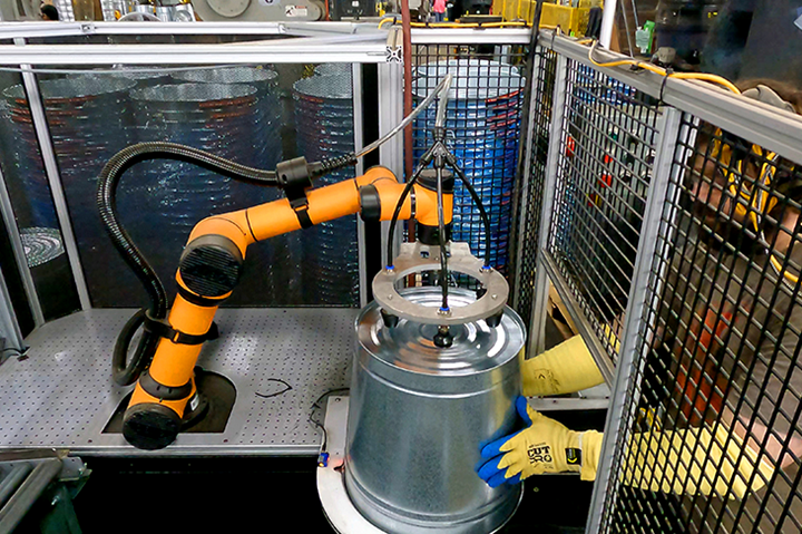 Cobot tends a machine that pierces holes into a metal pail